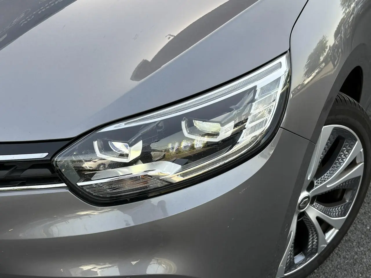 Gros plan sur le phare avant droit et la jante alliage du Renault Grand Scenic IV gris Cassiopée.