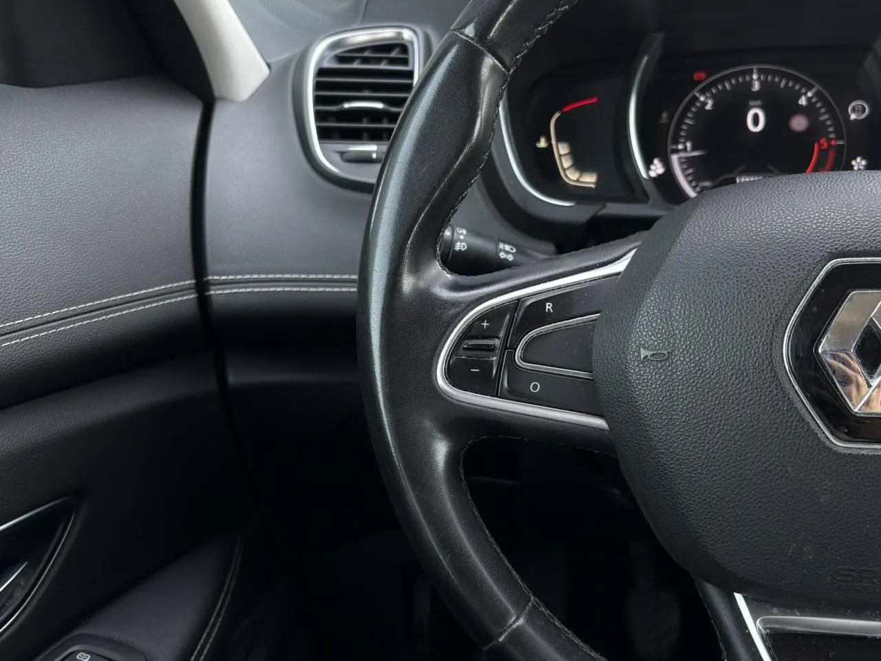 Gros plan sur le volant cuir noir et le tableau de bord digital du Renault Grand Scenic IV, ambiance intérieure sombre.