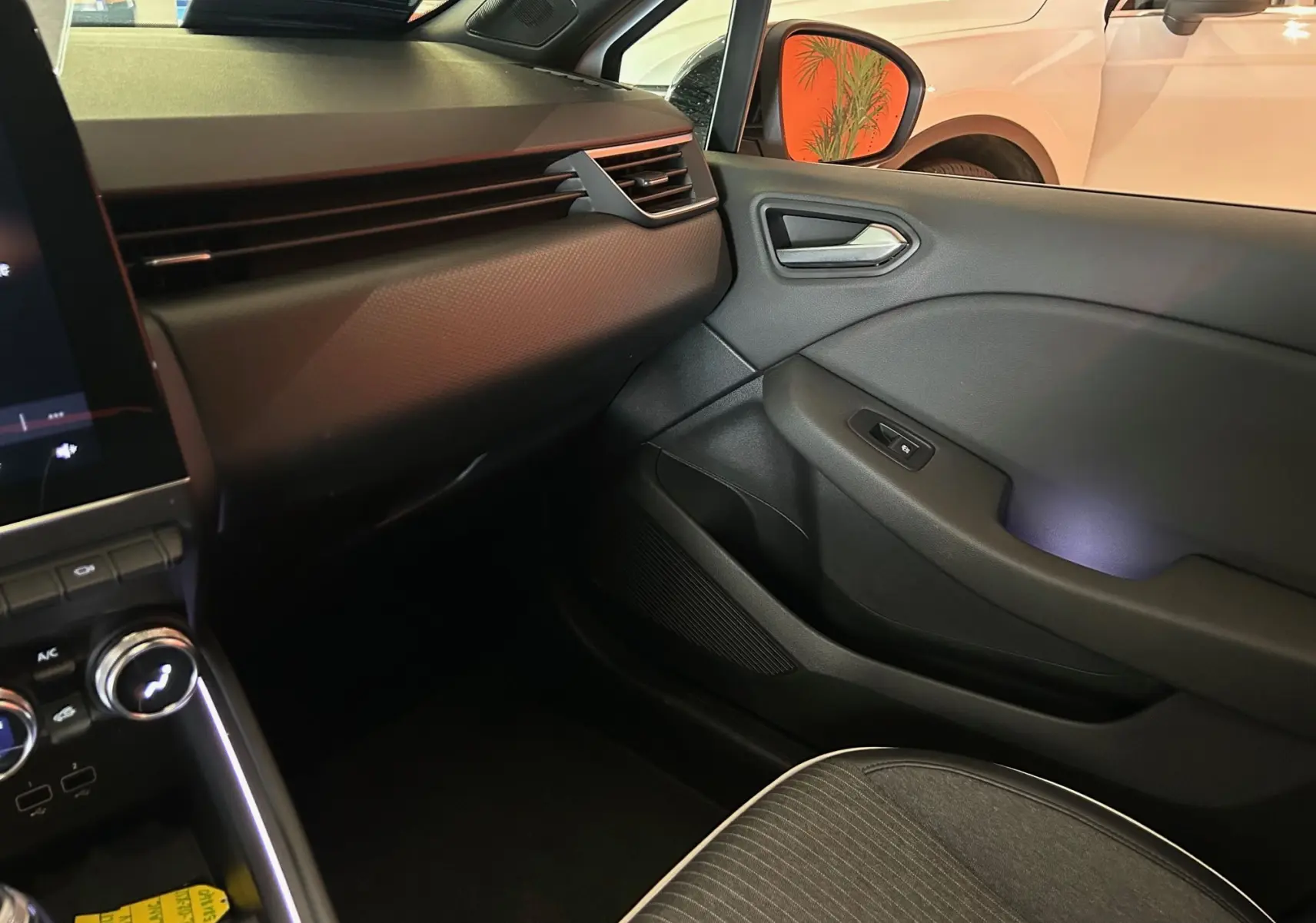 Intérieur côté passager de la Renault Clio V blanc nacré, montrant la portière et la partie basse du tableau de bord.