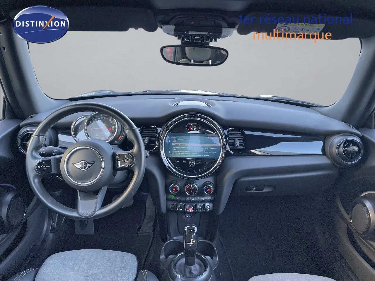 Vue intérieure du tableau de bord et volant noir d'une MINI Cabriolet F57 2023 avec écran central rond et commandes climatiques.