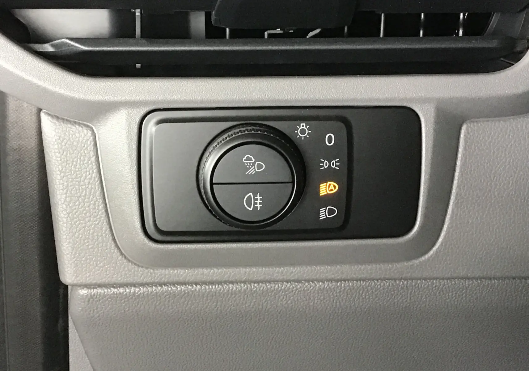 Gros plan sur le bouton de commande des phares du Volkswagen Transporter gris anthracite, avec témoin orange allumé.