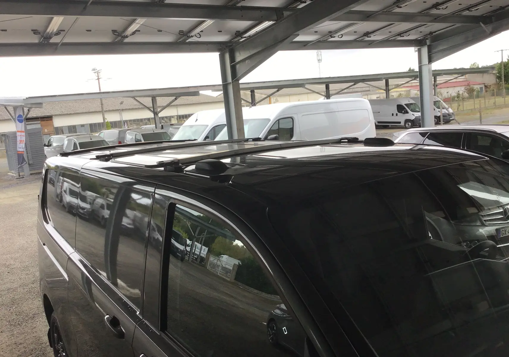 Vue en plongée du côté gauche d'un Volkswagen Transporter T7 gris anthracite avec barres de toit repliables sous abri.