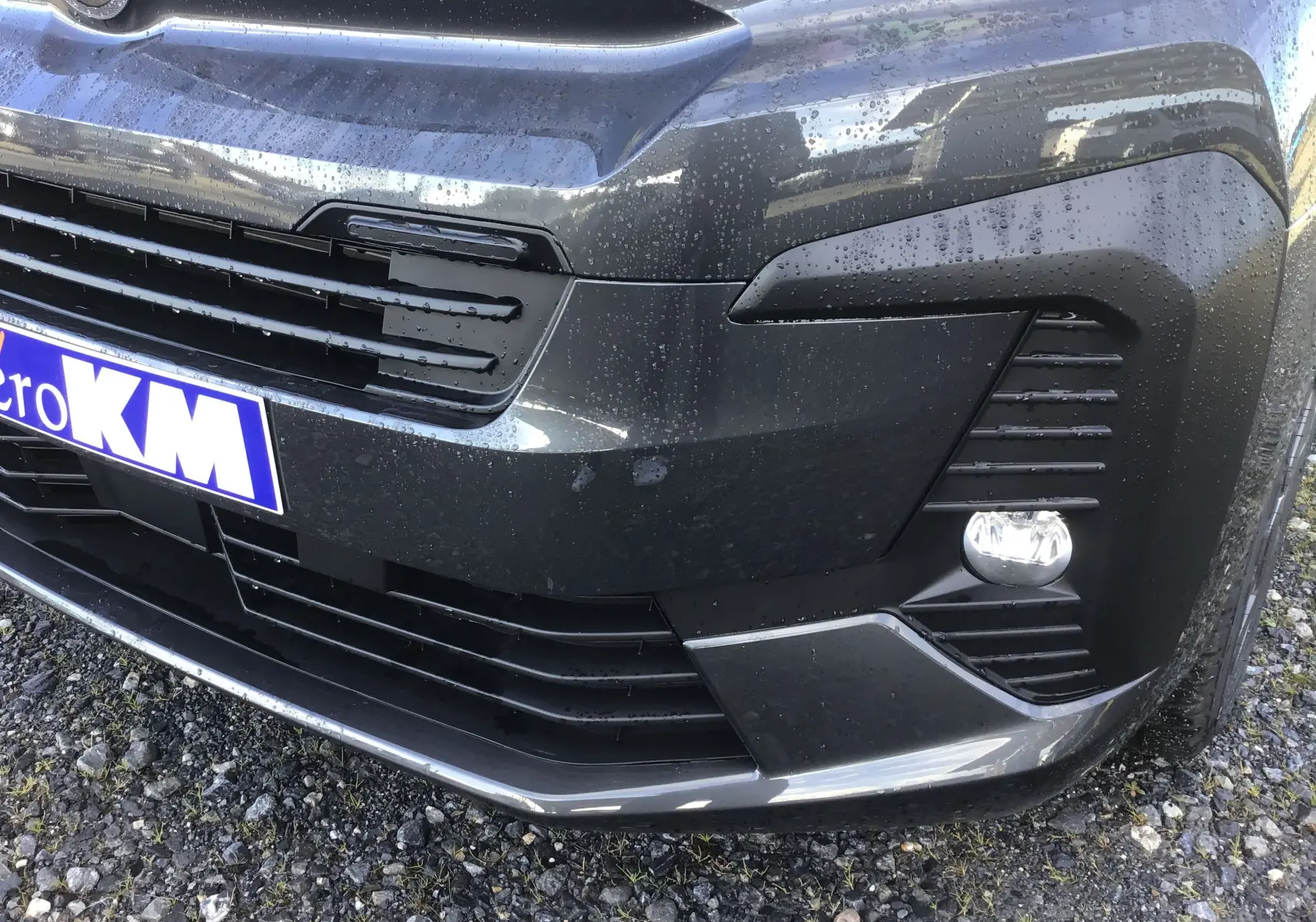 Gros plan sur l'avant droit gris titane du Citroën Jumpy XL avec calandre et antibrouillard sous la pluie.