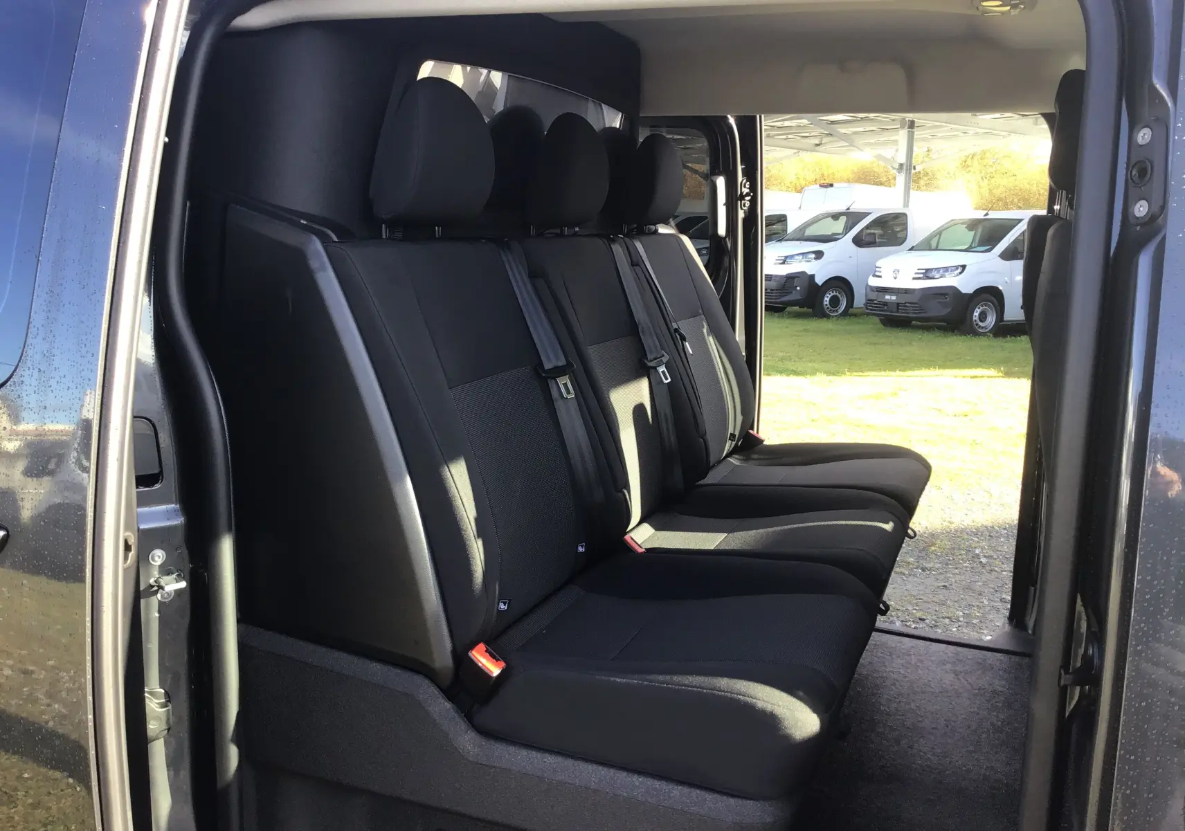 Vue latérale intérieure sur les sièges noirs du Citroën Jumpy Cabine Approfondie gris titane avec porte coulissante ouverte.