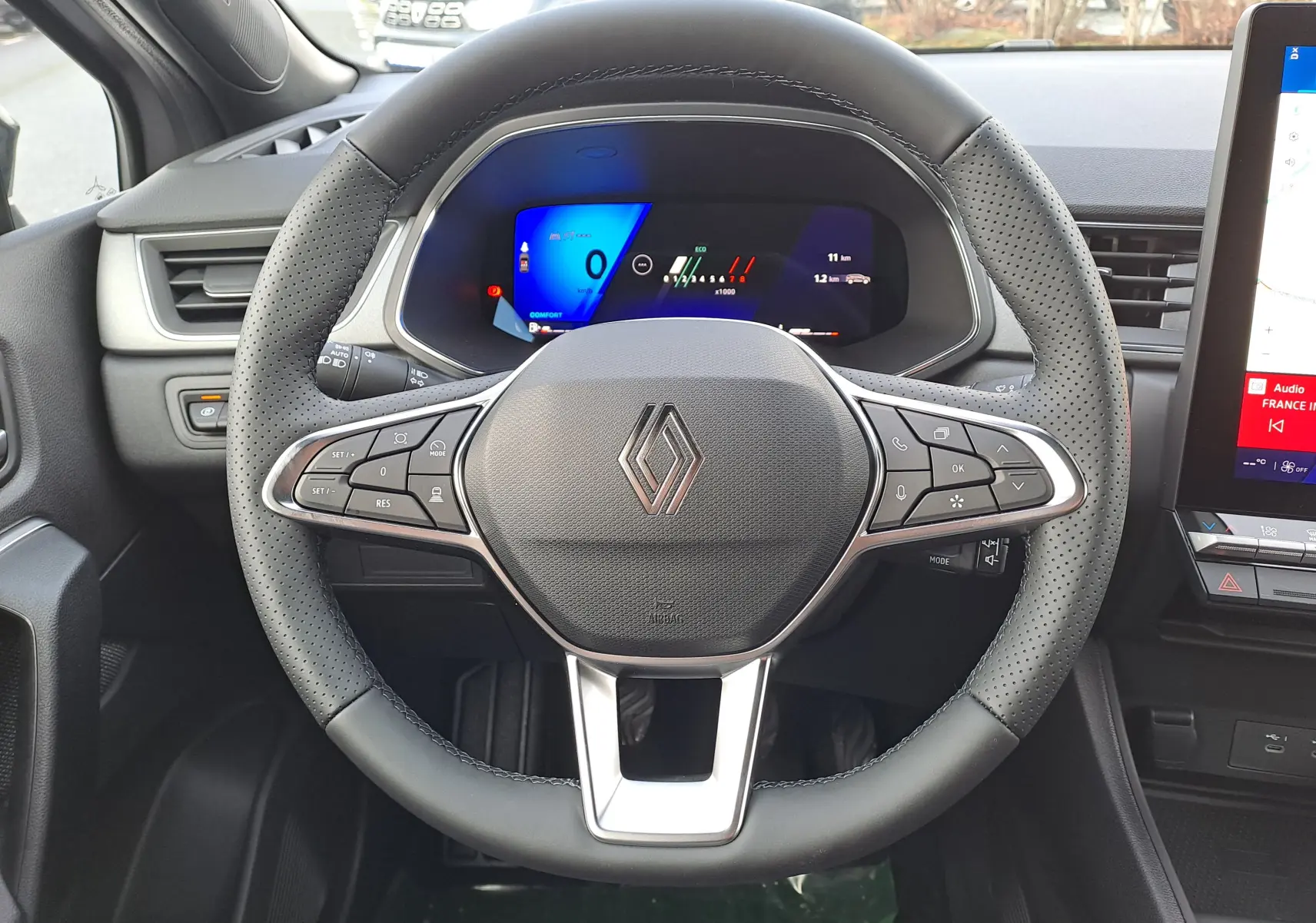 Vue centrée sur le volant noir perforé et le tableau de bord numérique lumineux de la Renault Symbioz gris cassiopée.