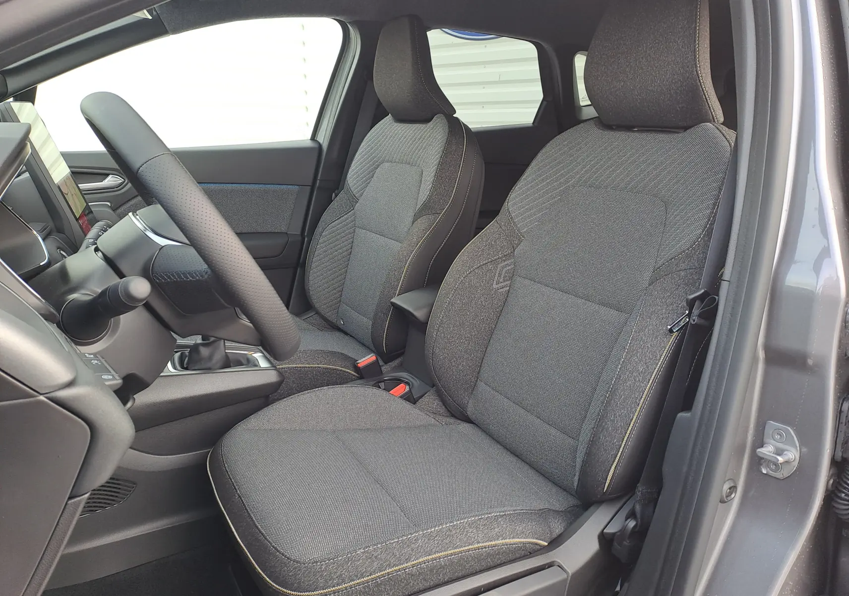 Vue intérieure côté gauche montrant les sièges avant gris foncé et le volant du Renault Symbioz Mild Hybrid 2025.