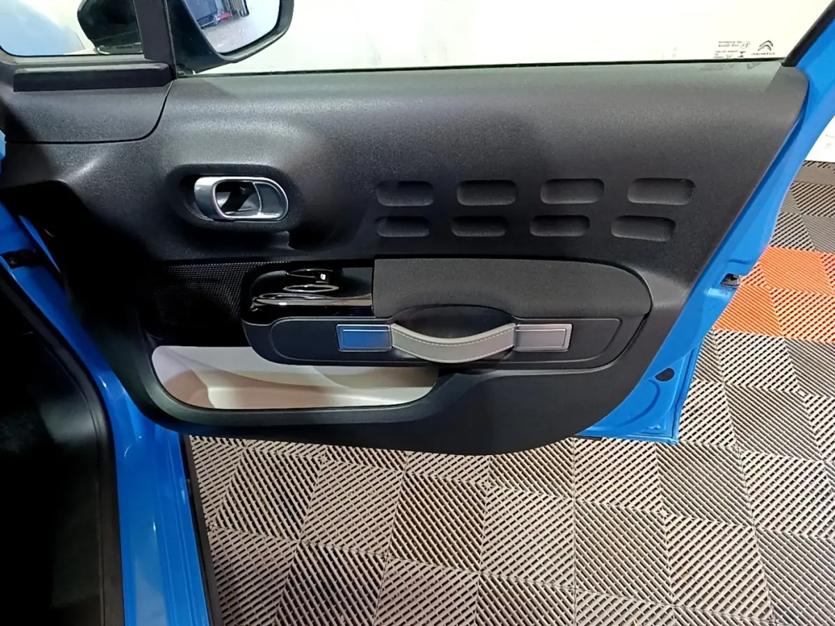 Vue rapprochée de la porte avant gauche bleu vif d'une Citroën C3 avec poignée intégrée et panneau noir texturé.