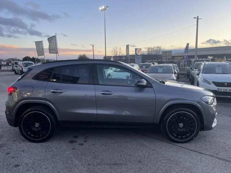 Vue de profil côté gauche d’un Mercedes GLA 250 e AMG Line gris foncé métal avec jantes noires, en extérieur au crépuscule.