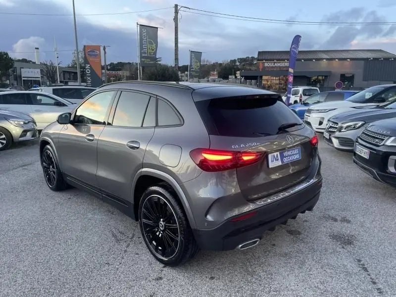 Vue 3/4 arrière droite d'une Mercedes GLA 250 e AMG Line gris foncé métal avec feux allumés sur parking.