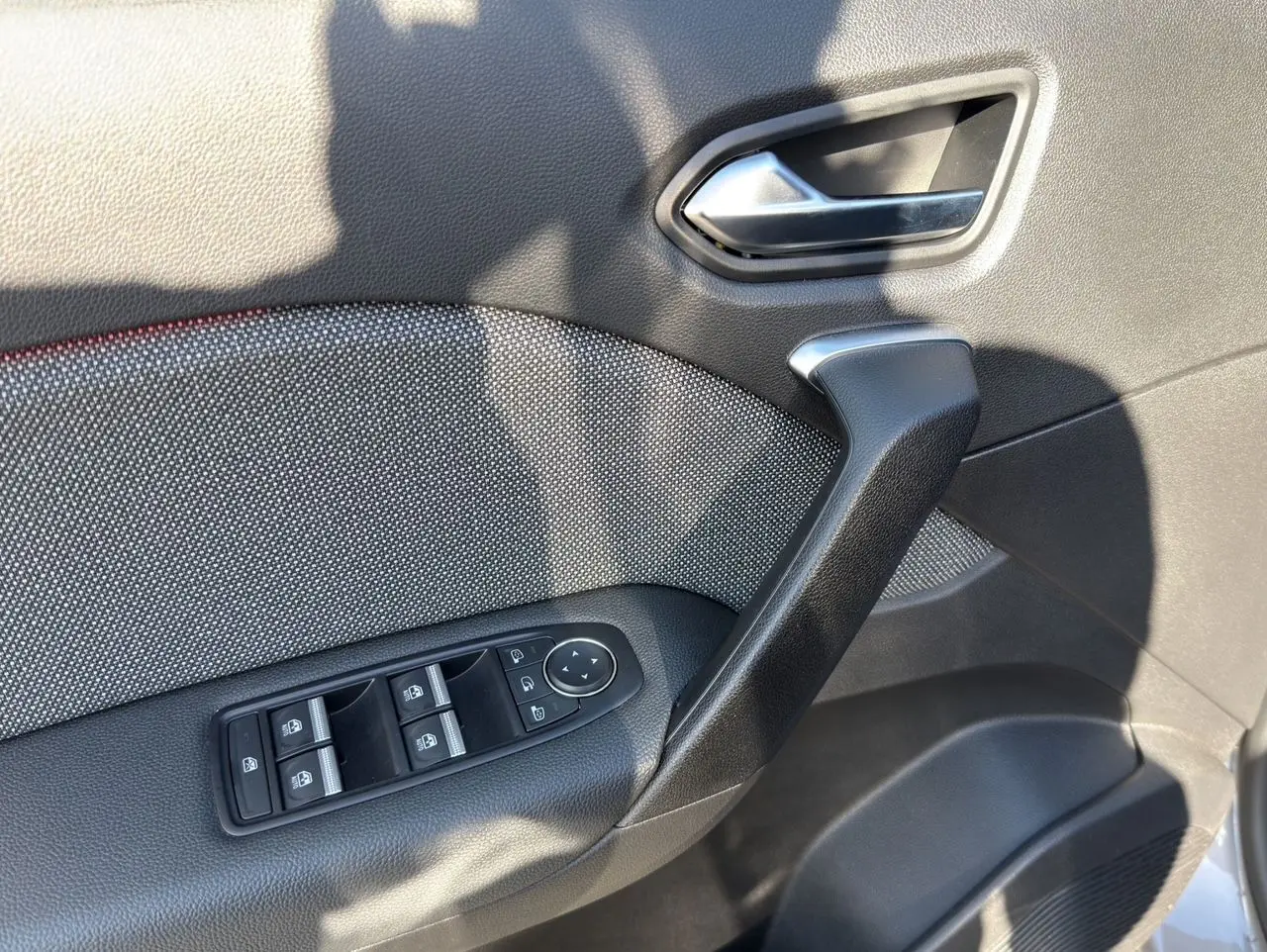 Gros plan sur la porte avant gauche du Renault Captur gris Cassiopée, montrant la poignée, les commandes des vitres et le revêtement tissu noir.
