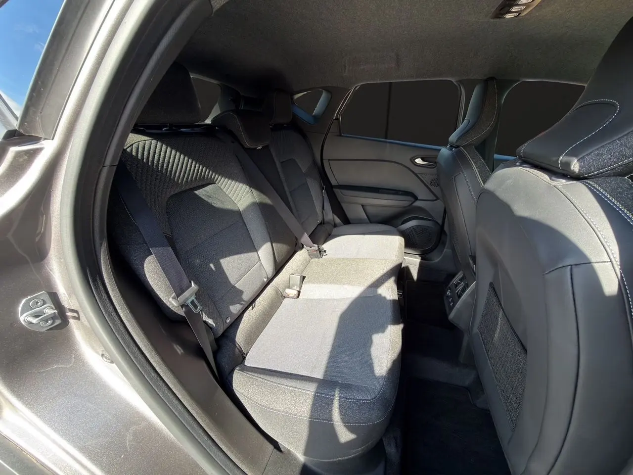 Vue intérieure côté gauche des sièges arrière gris tissu et cuir du Renault Captur TCe 90 Techno 2024 avec ceinture de sécurité visible.