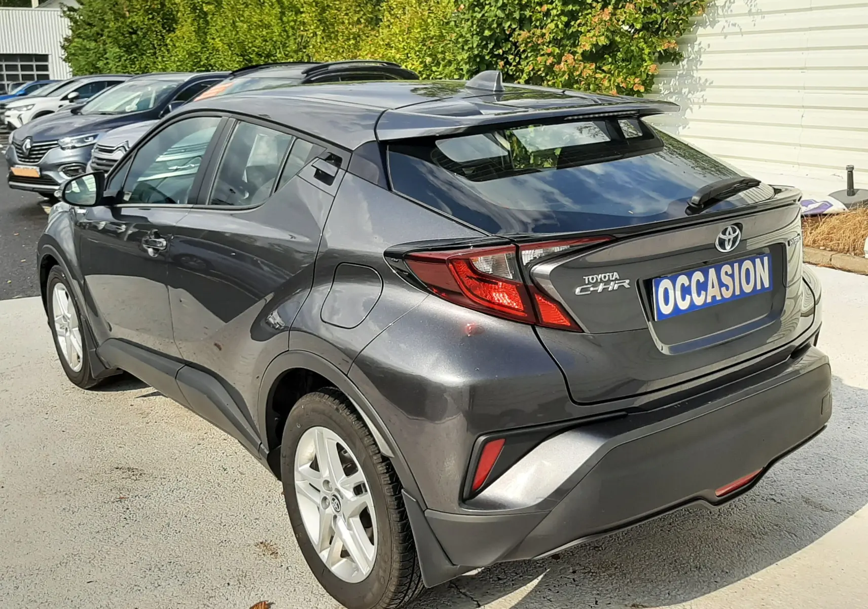 Toyota C-HR 1.8 Hybrid gris atlas métal vu en 3/4 arrière droit avec feux LED et toit noir contrasté.