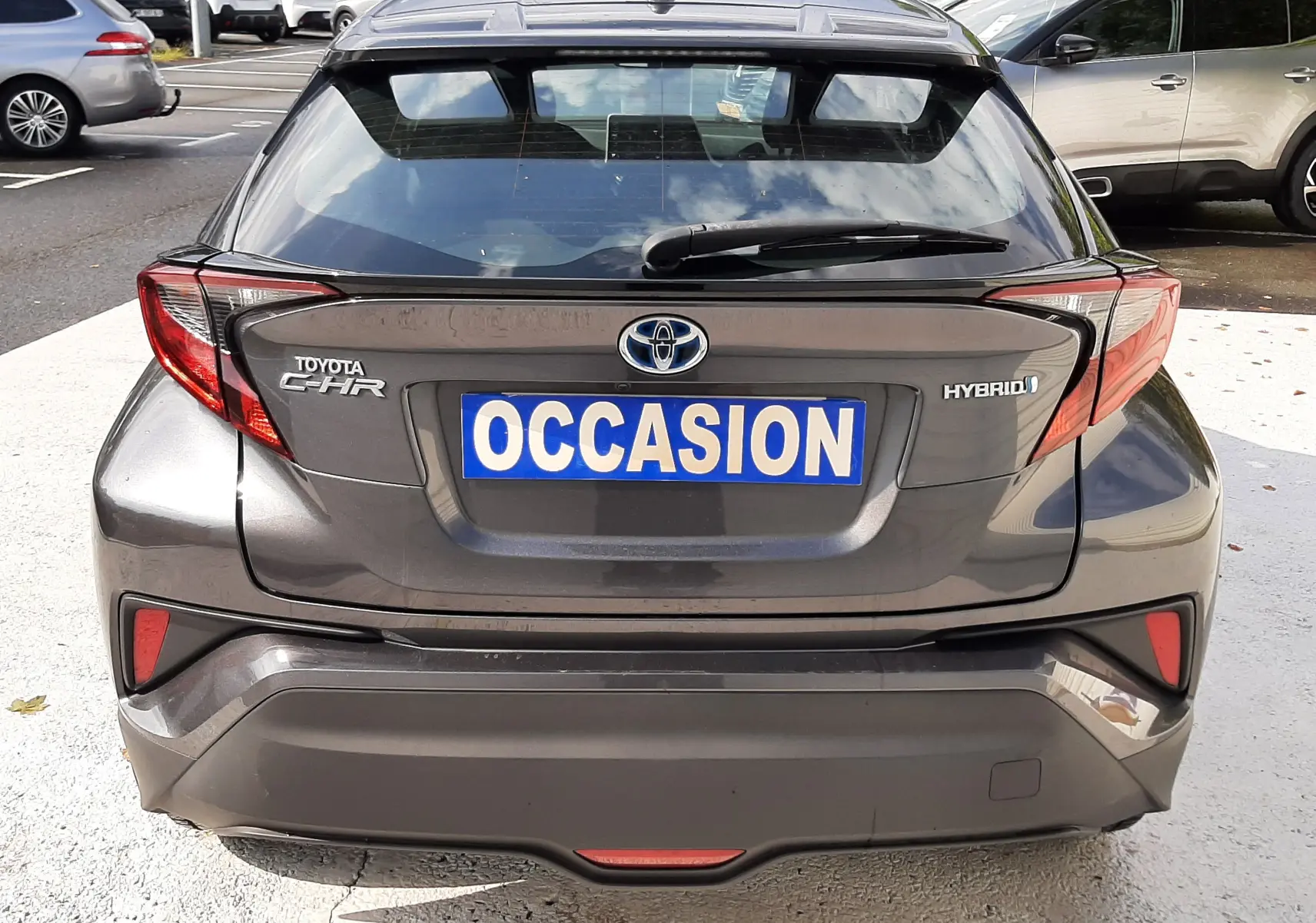 Vue arrière d'un Toyota C-HR gris atlas métal avec plaque "OCCASION" et feux arrière anguleux distinctifs.