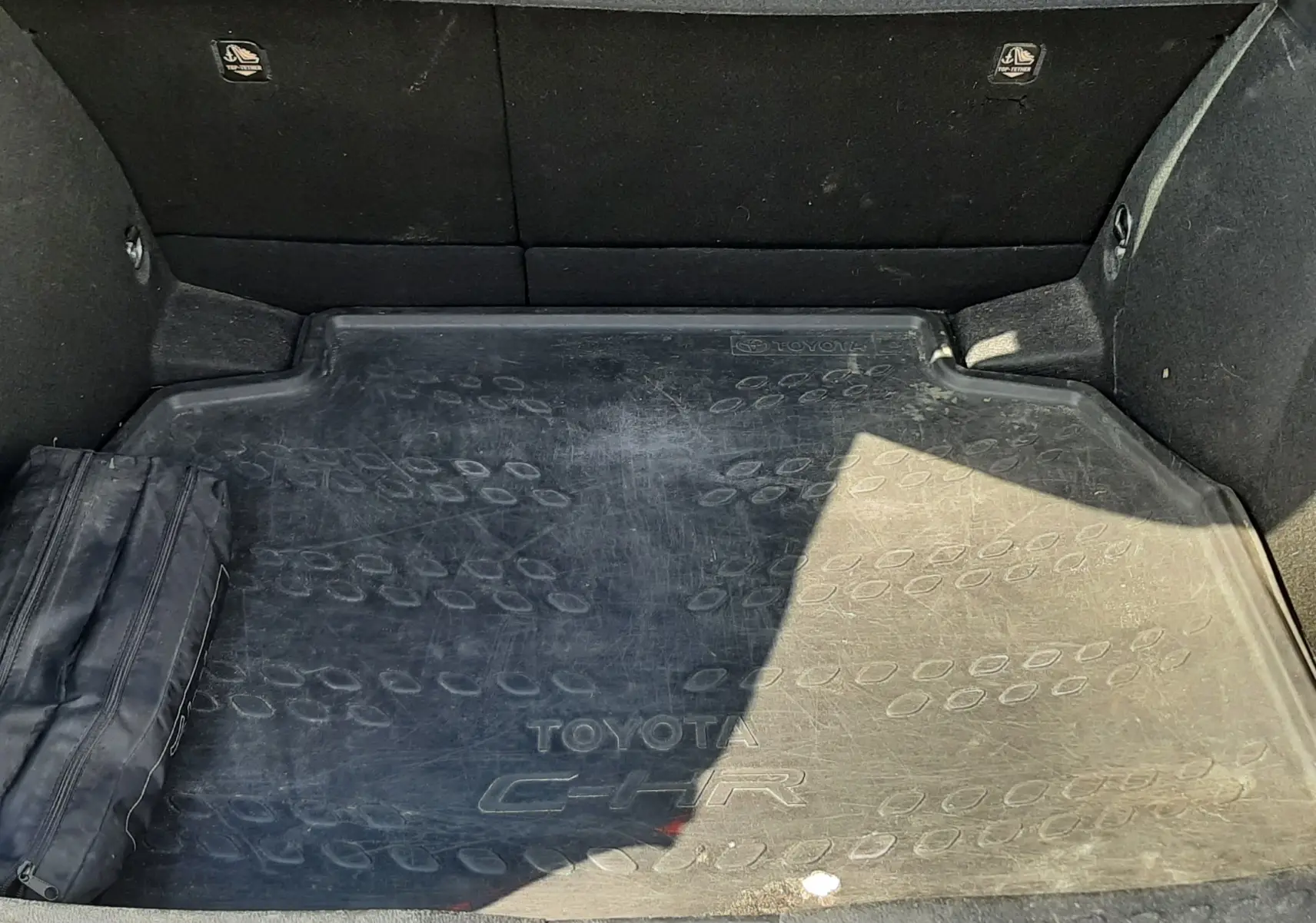 Vue du coffre du Toyota C-HR gris atlas, avec tapis de protection marqué du logo et dossier arrière en tissu gris.