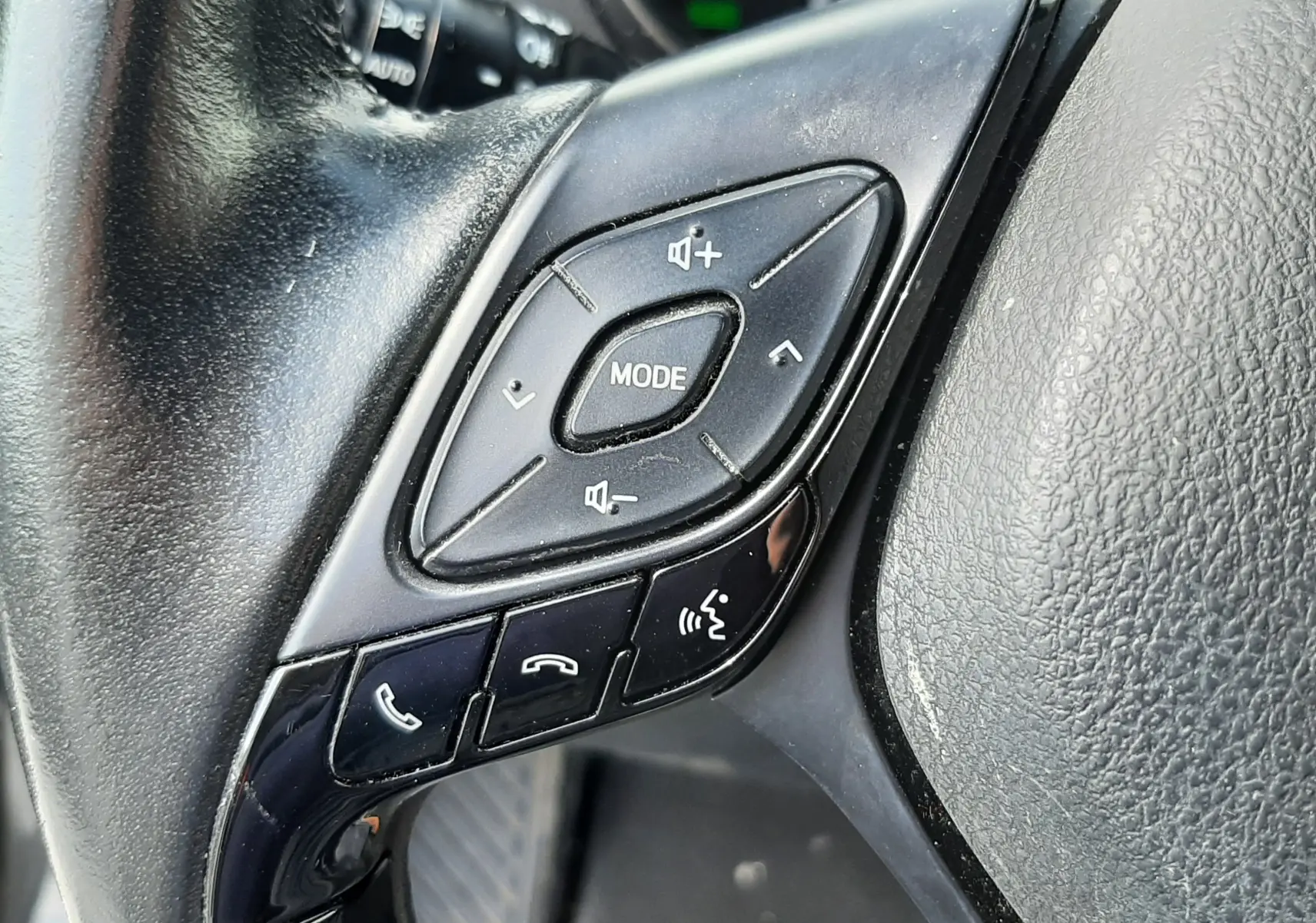 Gros plan sur les commandes multifonctions noires du volant du Toyota C-HR 1.8 Hybrid 2021, intérieur gris.