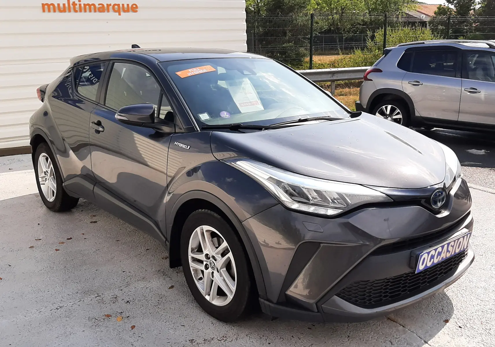 Toyota C-HR 1.8 Hybrid gris atlas métal vu en 3/4 avant droit, avec jantes alliage et feux LED distinctifs.