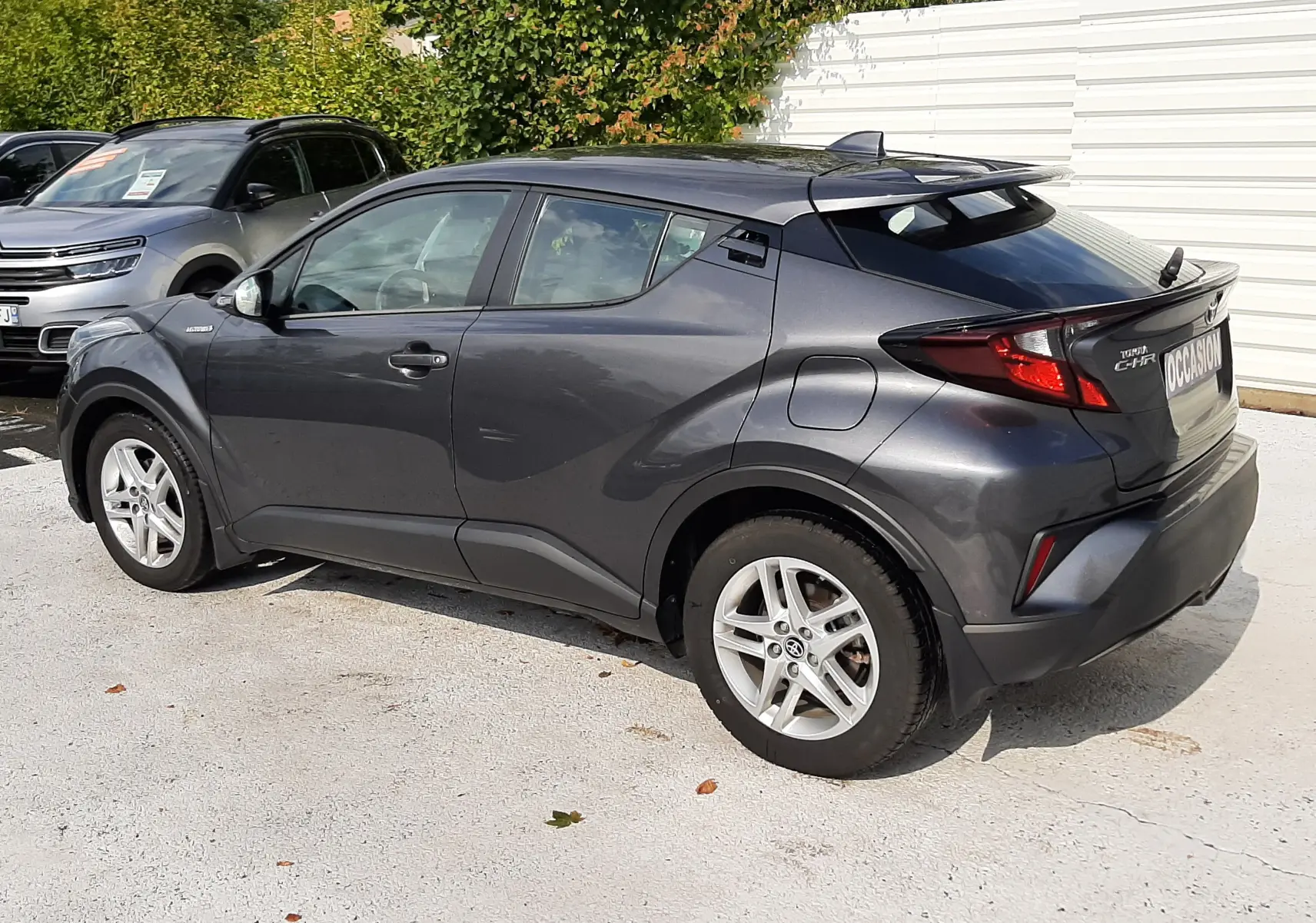Toyota C-HR 1.8 Hybrid gris atlas métal vu de trois quarts arrière droit, avec jantes alliage et toit noir.
