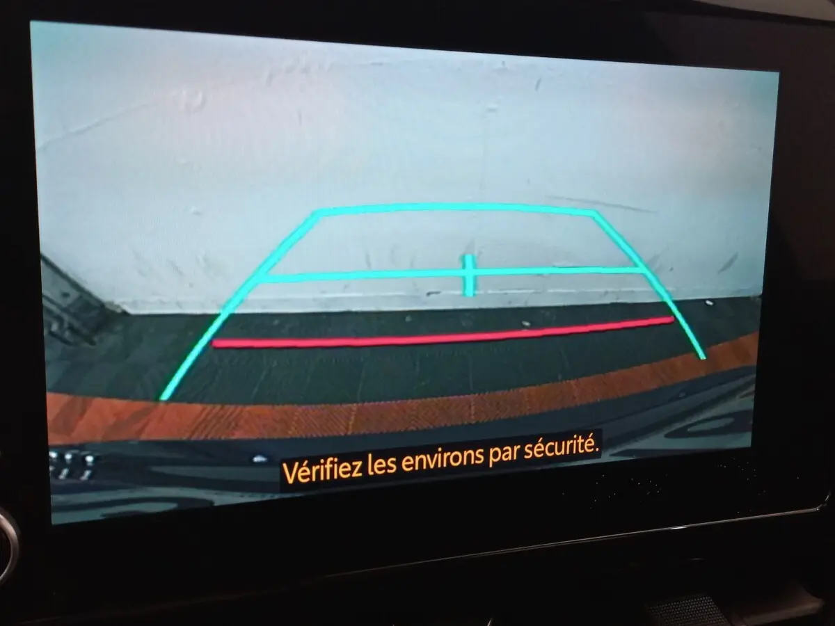 Vue de la caméra de recul d'une Toyota Corolla hybride bleue, avec lignes de guidage colorées à l'écran.