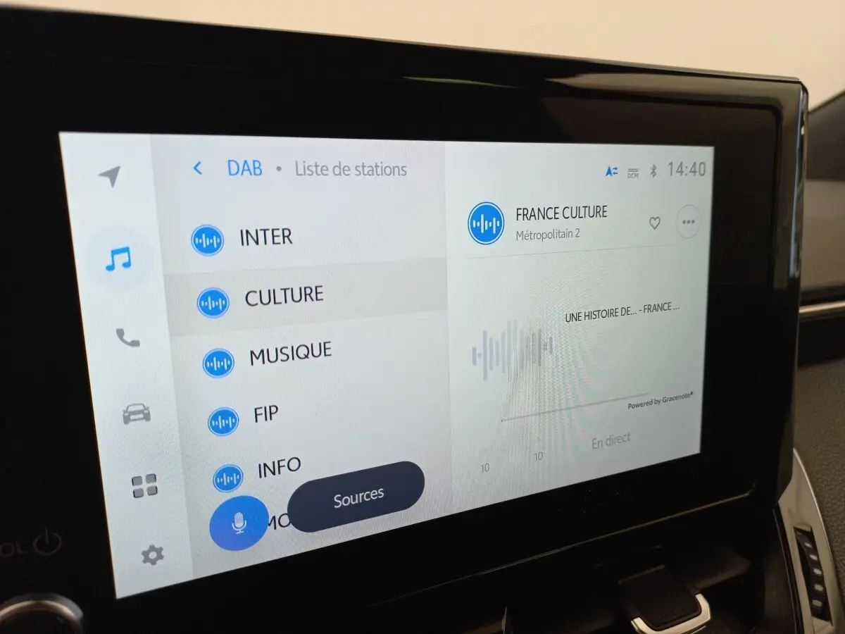 Écran tactile central de la Toyota Corolla hybride 2022 affichant la liste des stations radio en intérieur.