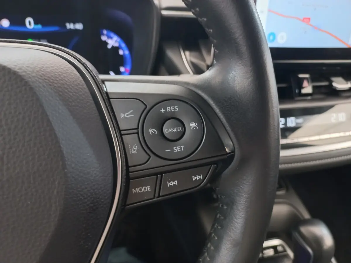 Gros plan sur le volant cuir noir multifonctions de la Toyota Corolla hybride, avec tableau de bord et écran tactile en arrière-plan.