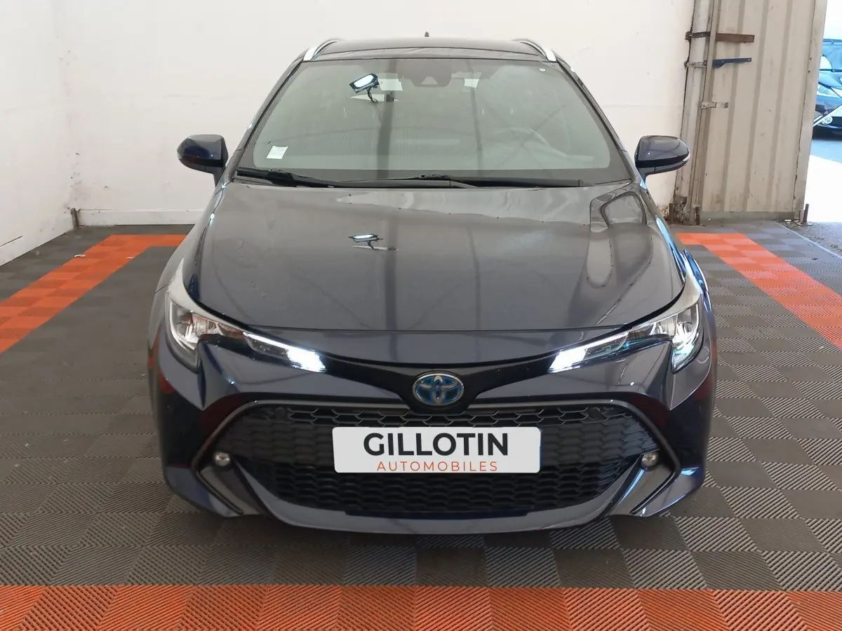 Vue avant d'une Toyota Corolla hybride bleu foncé avec calandre noire et phares LED allumés dans un garage.