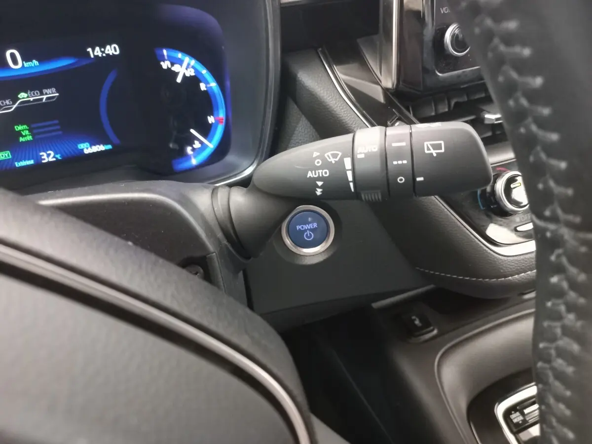 Vue intérieure rapprochée du tableau de bord et du volant cuir d'une Toyota Corolla hybride avec bouton Power bleu et affichage digital.