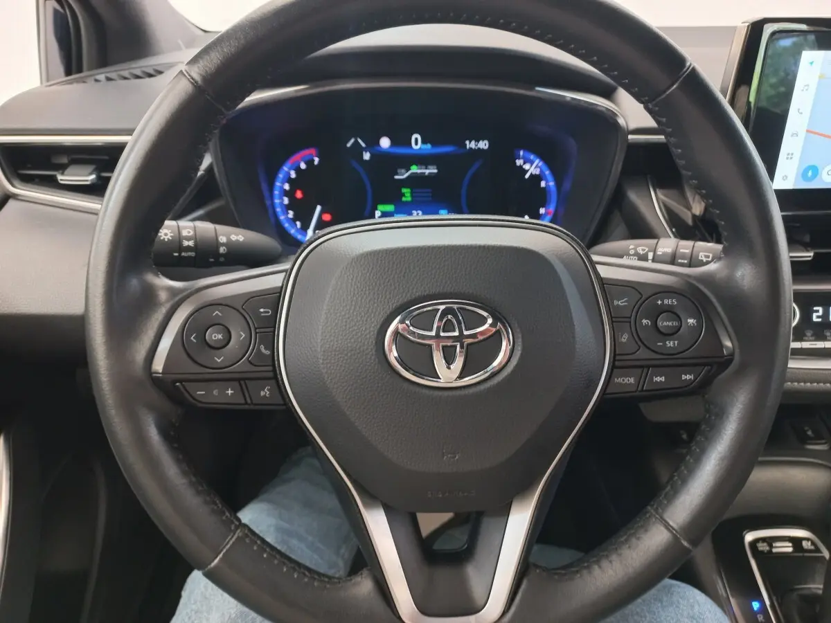 Vue rapprochée du volant cuir multifonctions noir d'une Toyota Corolla hybride 2022 avec tableau de bord digital éclairé.