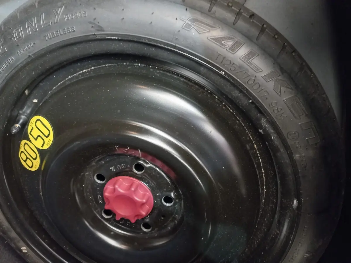 Gros plan sur la roue de secours noire avec bouchon rouge et pneu Falken visible sur une Toyota Corolla hybride bleue.