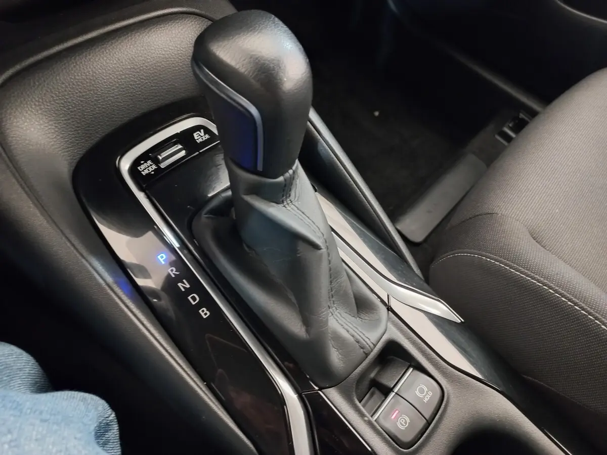 Gros plan sur la console centrale noire avec levier de vitesse automatique en cuir et boutons mode conduite et frein à main électrique.