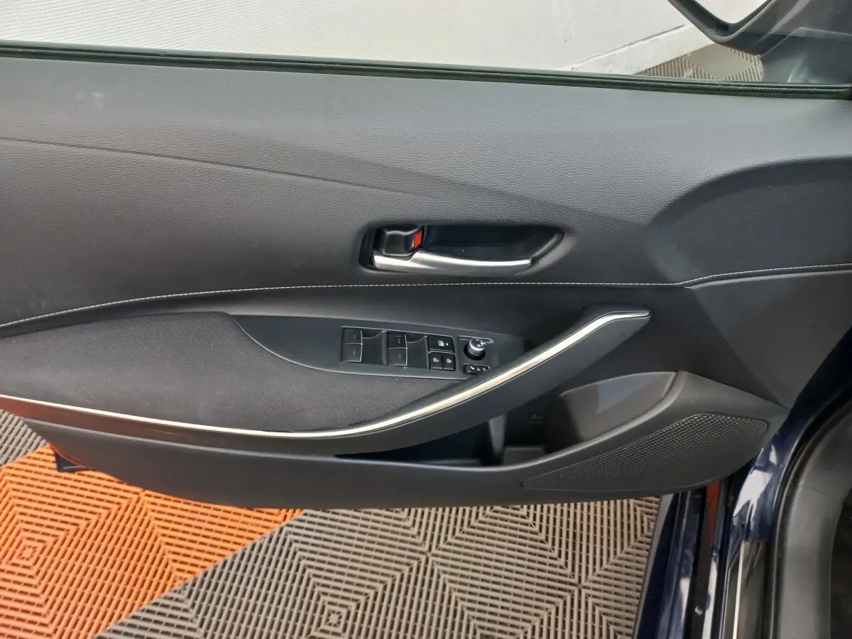Vue intérieure côté gauche de la porte avant bleu foncé d'une Toyota Corolla hybride avec commandes de vitres et poignée argentée.
