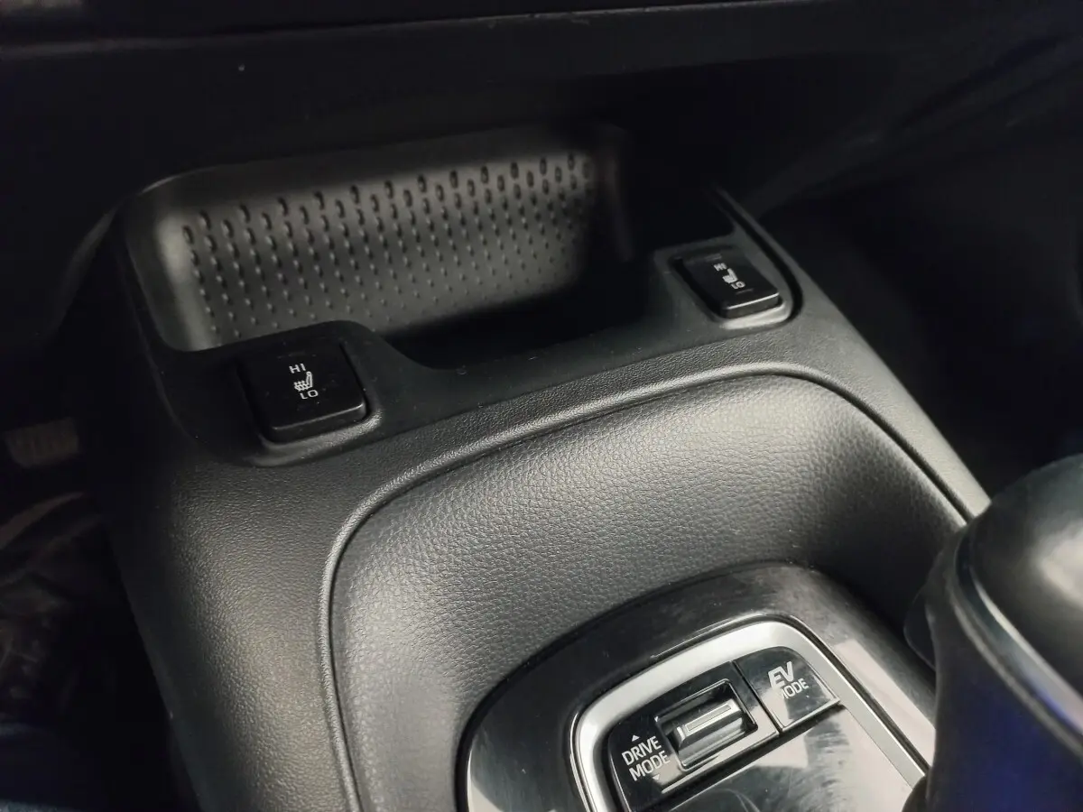 Gros plan sur la console centrale noire de la Toyota Corolla hybride 2022, avec commandes chauffantes et modes de conduite.