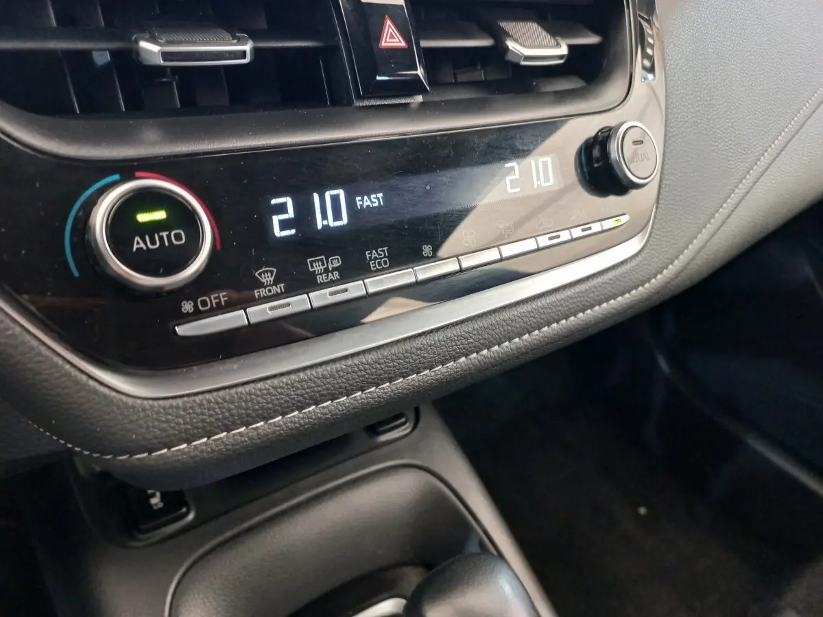 Gros plan sur la console centrale noire de la Toyota Corolla hybride, affichant la climatisation digitale à 21°C.