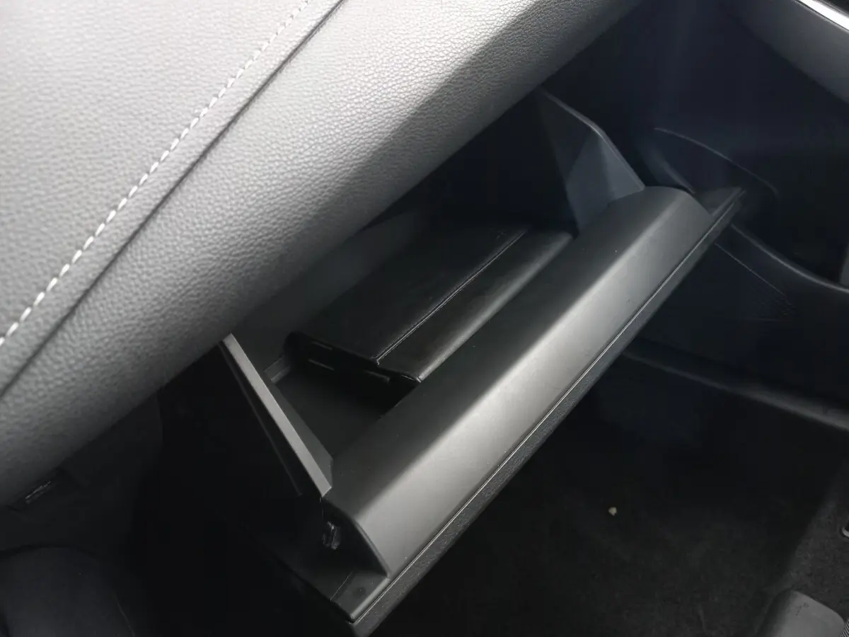 Gant de boîte à gants ouvert côté passager avec livret noir dans l’habitacle sombre d’une Toyota Corolla hybride bleue.