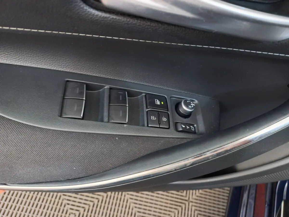Vue rapprochée des commandes de lève-vitres et rétroviseurs sur la porte côté conducteur d'une Toyota Corolla hybride bleue.