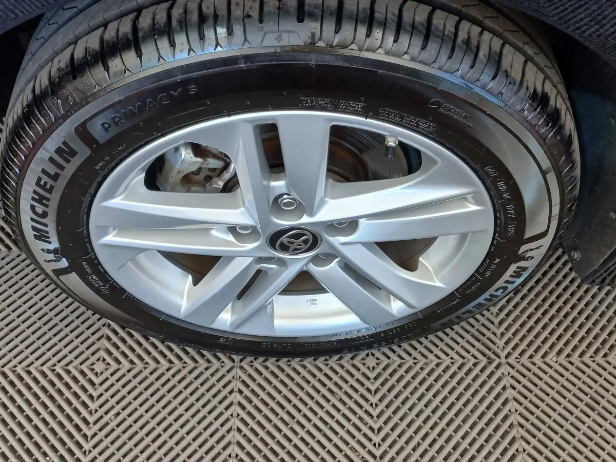 Gros plan sur la jante alliage argentée avec logo Toyota, pneu Michelin, sol en damier sous la roue.