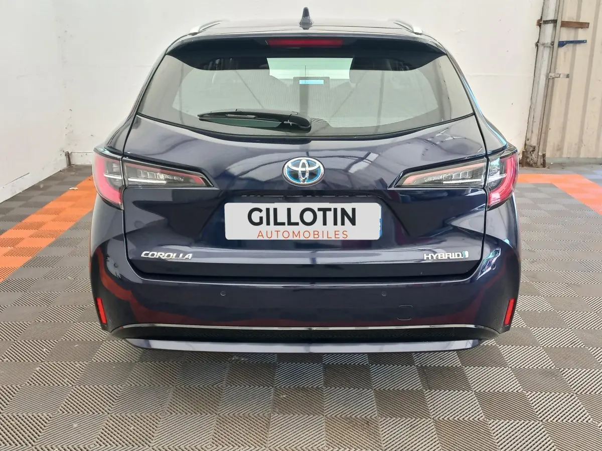 Vue arrière d'une Toyota Corolla hybride bleu foncé avec logo et badges visibles dans un showroom intérieur.