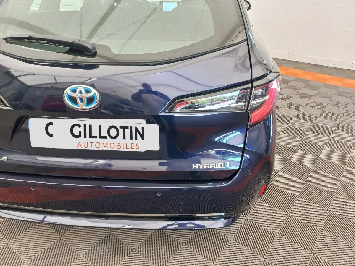 Vue arrière droite d'une Toyota Corolla hybride bleu foncé avec logo Hybrid et plaque d'un concessionnaire.