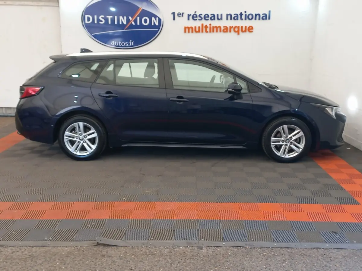 Profil côté gauche d'une Toyota Corolla break hybride bleu foncé, avec jantes alliage et toit blanc en intérieur showroom.