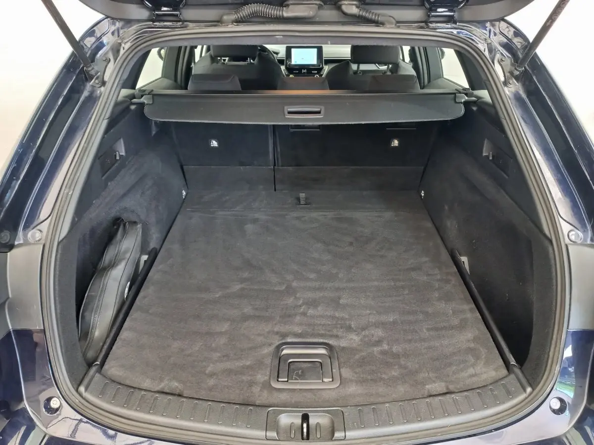 Coffre ouvert vu de l'arrière d'une Toyota Corolla hybride bleu, avec banquette arrière et écran tactile visibles.