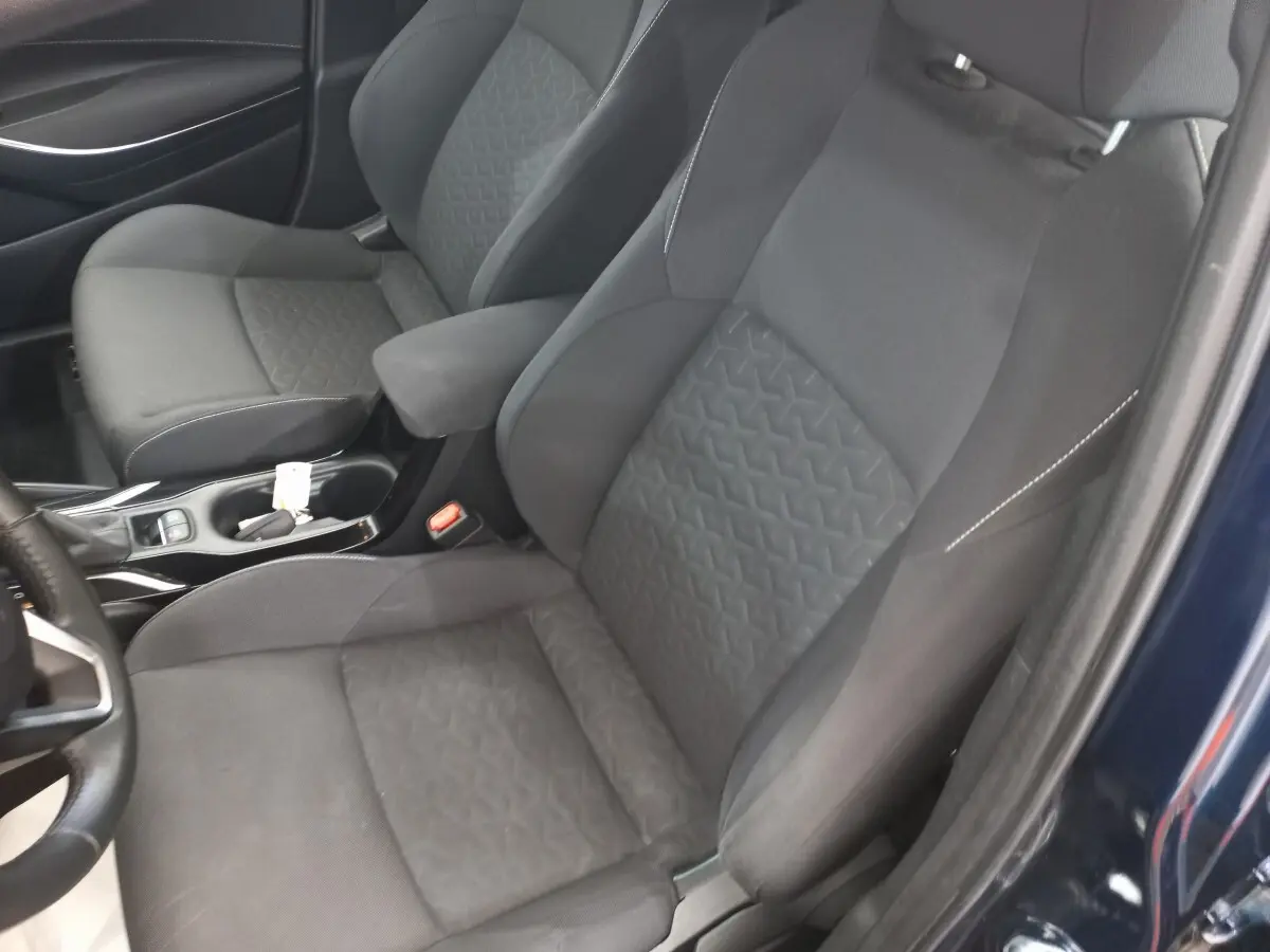 Vue intérieure rapprochée des sièges avant noirs et de l'accoudoir dans une Toyota Corolla hybride bleue 2022.