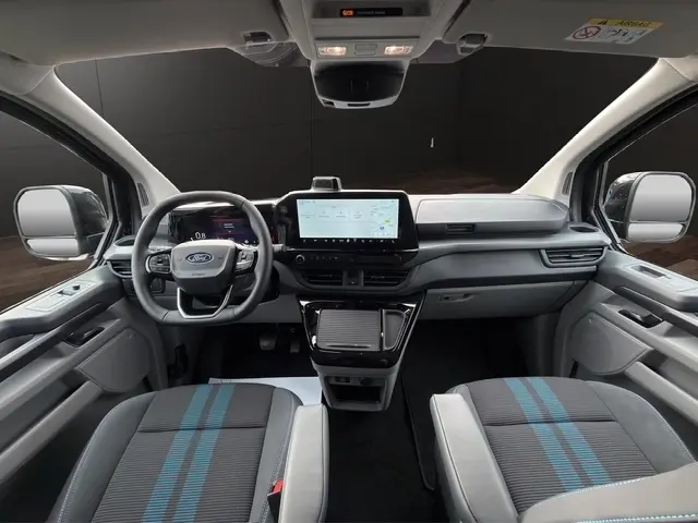Vue intérieure avant du Ford Transit Fourgon 2026, tableau de bord moderne avec écran tactile central et sièges gris à bandes bleues.