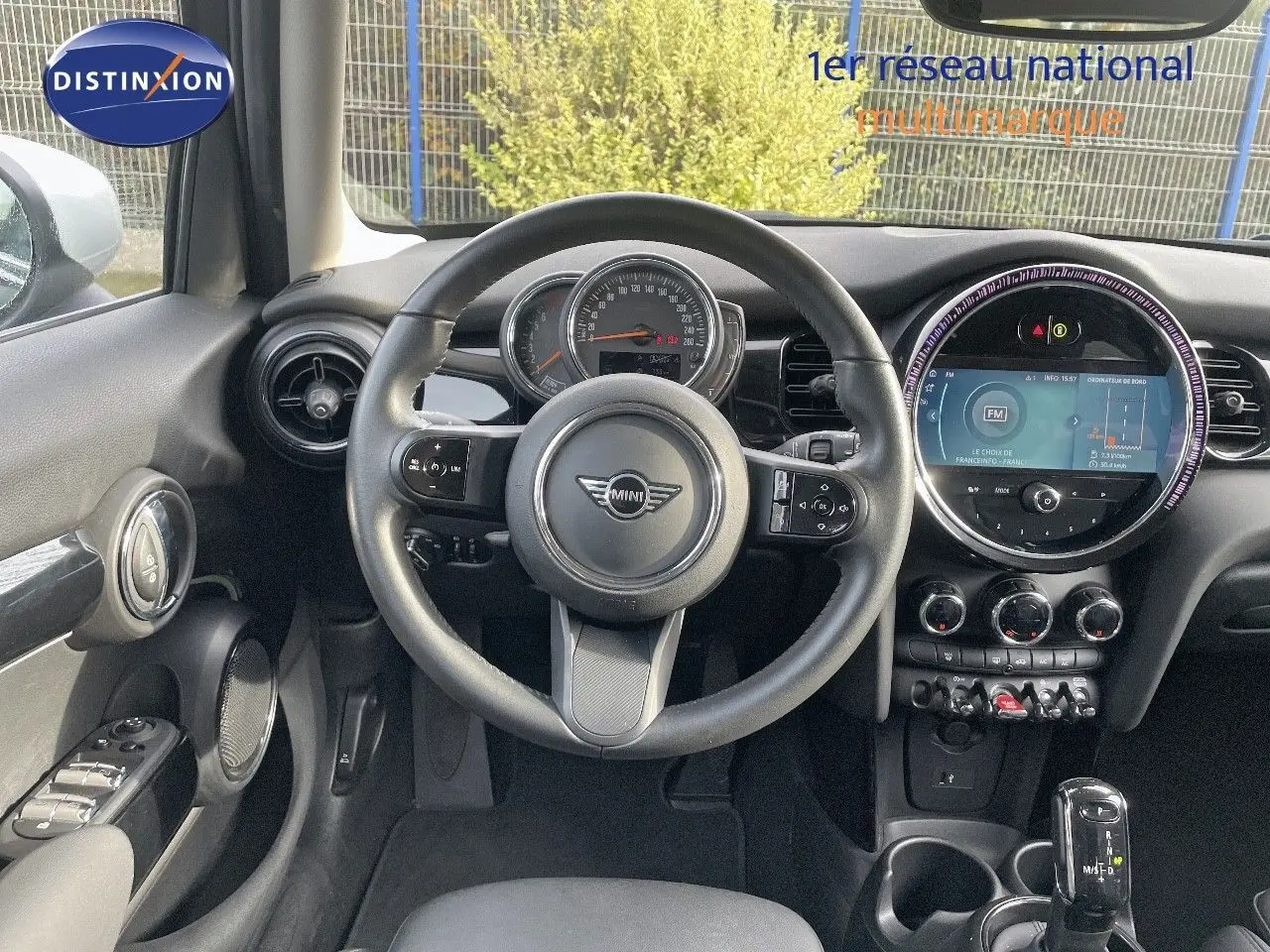 Vue intérieure centrée sur le volant et le tableau de bord de la MINI 1.5 136CH noir avec écran tactile rond et commandes au volant.
