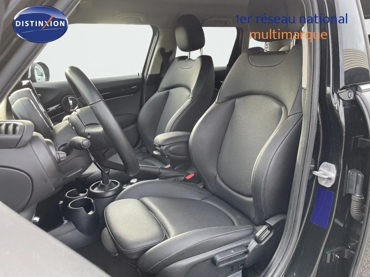 Vue intérieure côté conducteur d'une MINI 1.5 136CH noire, sièges en cuir noir avec console centrale et volant visibles.