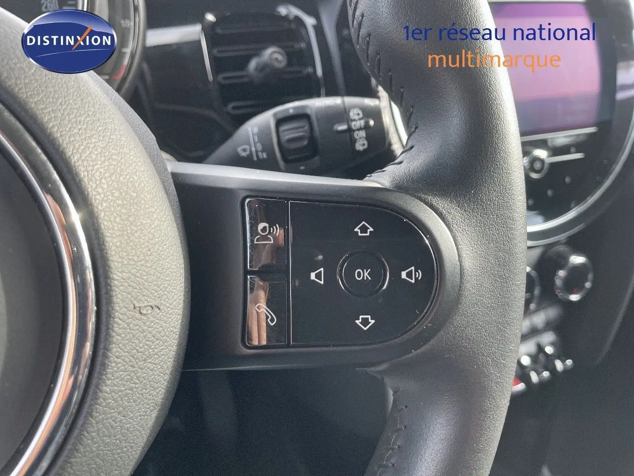 Gros plan sur les commandes multifonctions du volant en cuir noir d'une MINI 2023, avec tableau de bord flou en arrière-plan.