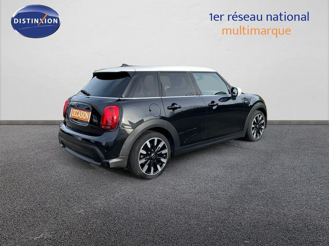 Vue 3/4 arrière droite d'une MINI noire Midnight Metal avec toit blanc et jantes bi-ton, stationnée sur sol gris.