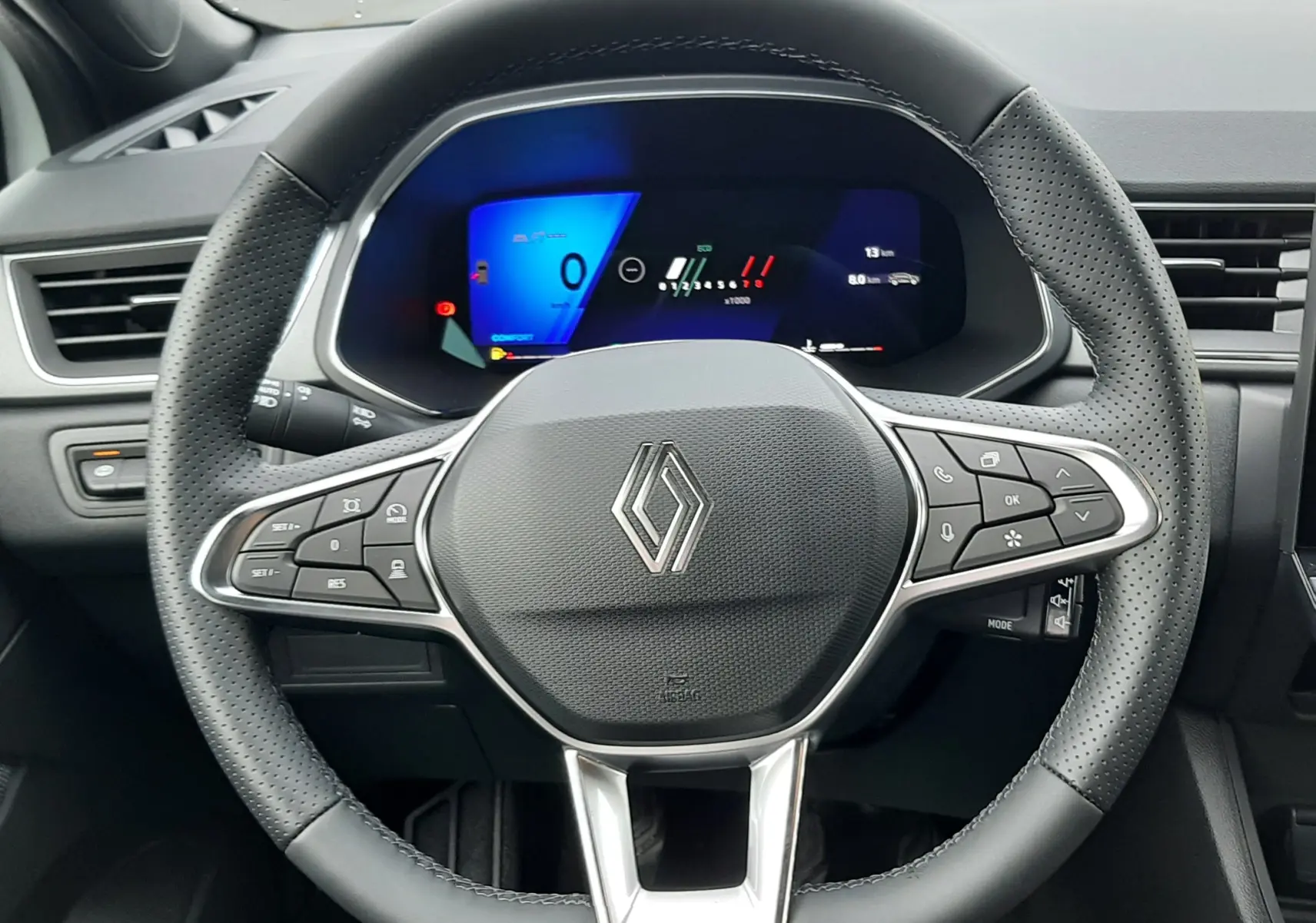 Vue intérieure centrée sur le volant noir perforé et le tableau de bord numérique lumineux d'une Renault Symbioz blanche nacrée.