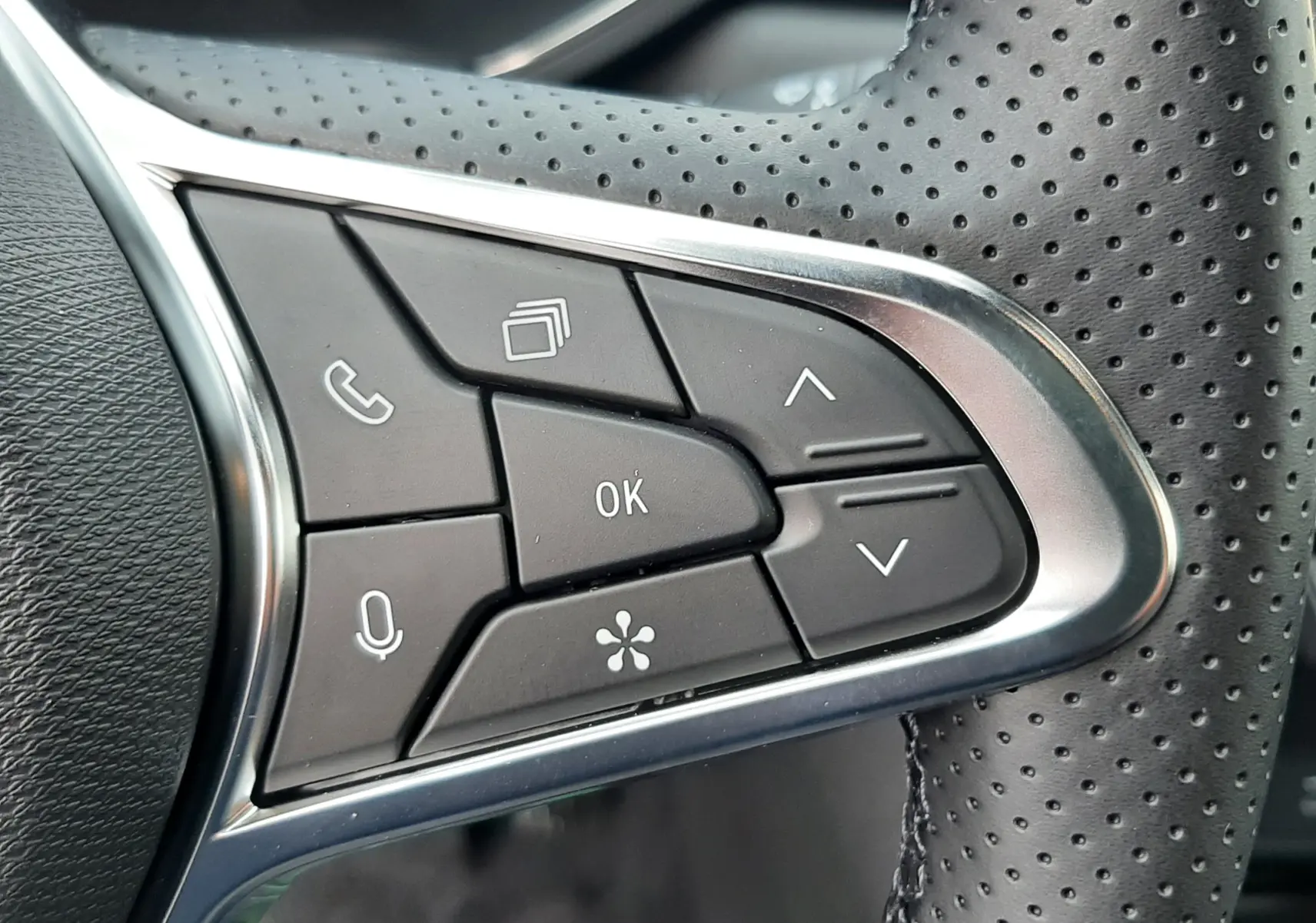 Gros plan sur les commandes multifonctions en plastique noir et chrome du volant perforé côté gauche du Renault Symbioz 2025.