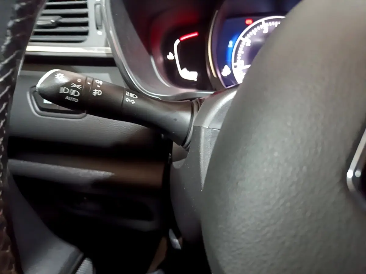 Gros plan sur la manette de commande des phares et clignotants à gauche du volant d’un Renault Kadjar noir, tableau de bord éclairé.