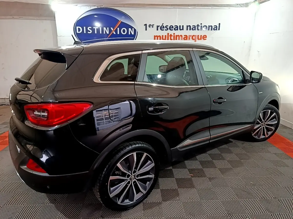 Vue 3/4 arrière droite du Renault Kadjar Intens noir brillant dans un showroom avec jantes alliage et vitres teintées.