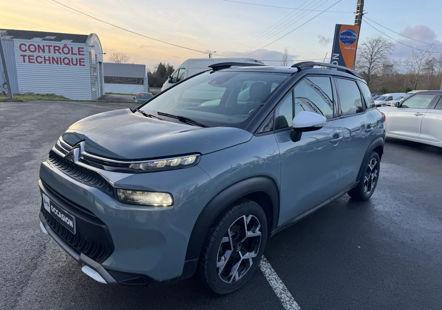 Vue 3/4 avant d'une Suzuki Swace hybride bleu foncé en showroom, avec calandre noire et jantes argentées.